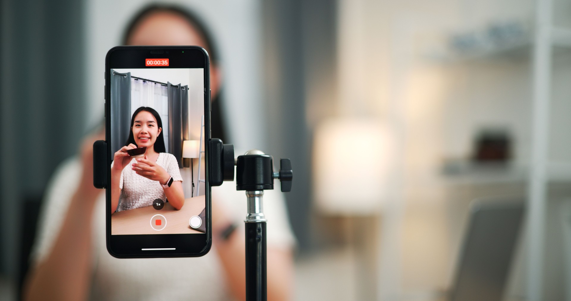 Close-up of a young woman selling ceramic plates, bowls, online by video using her smartphone at home.